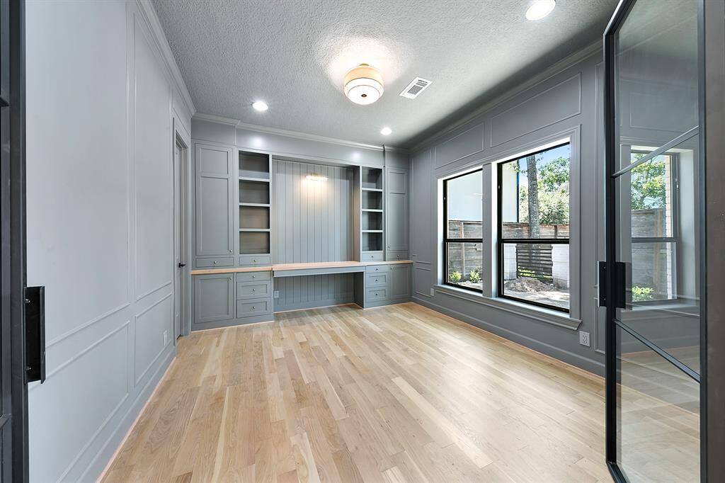 This home office features elegant built-in cabinetry, ample natural light from large windows, and stylish glass doors, creating a bright and functional workspace.
