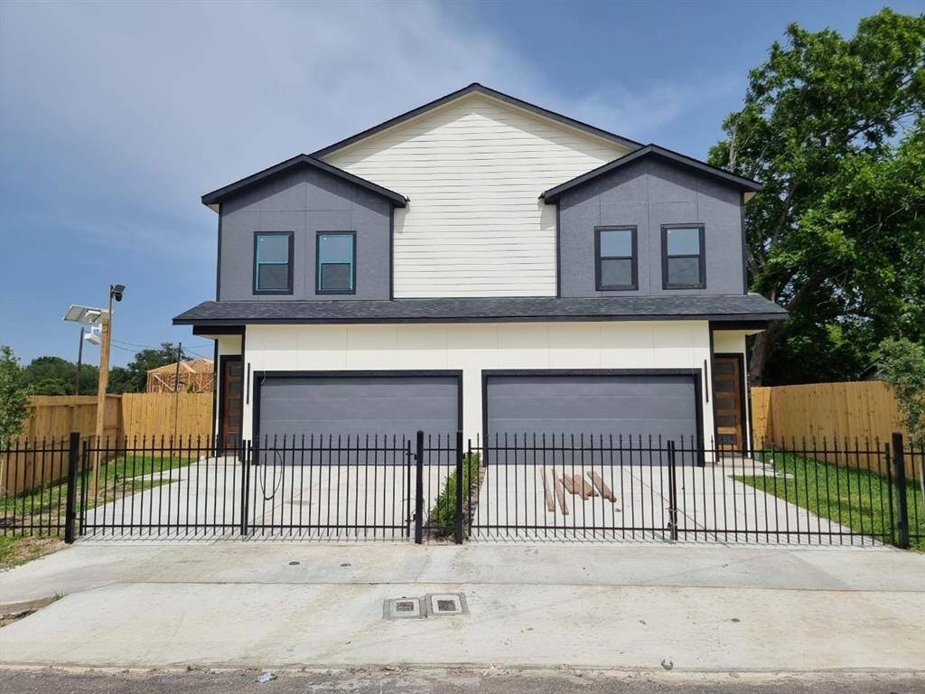 The front view of the duplex with a two-story design, featuring a clean, contemporary facade. Each unit has a double garage and a small fenced front yard. The exterior is a mix of dark and light siding, complemented by a neat concrete driveway.