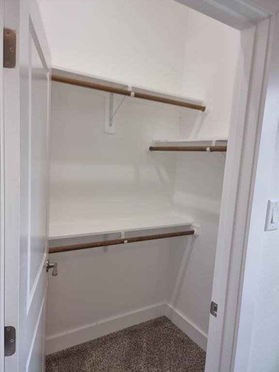 This is a small walk-in closet with built-in wooden shelves and rods. The walls are painted white, and the floor is carpeted, offering ample storage space in a compact area.