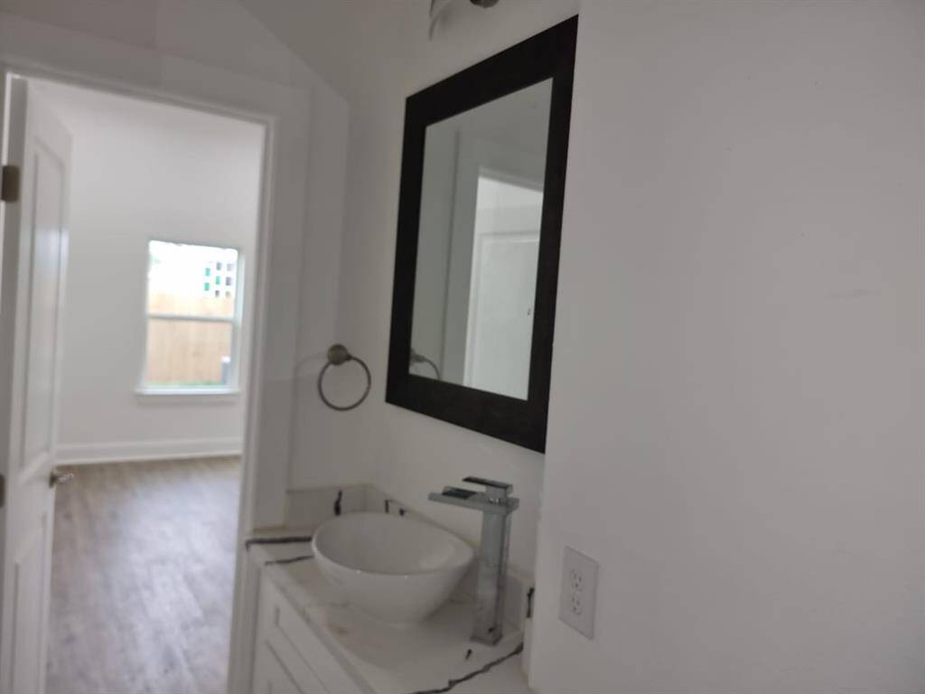 Bathroom with a vessel sink, sleek faucet, and a large mirror. Adjacent is a room with wood flooring and a window, offering natural light.