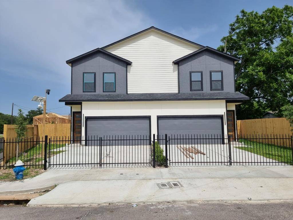 The front view of the duplex with a two-story design, featuring a clean, contemporary facade. Each unit has a double garage and a small fenced front yard. The exterior is a mix of dark and light siding, complemented by a neat concrete driveway.