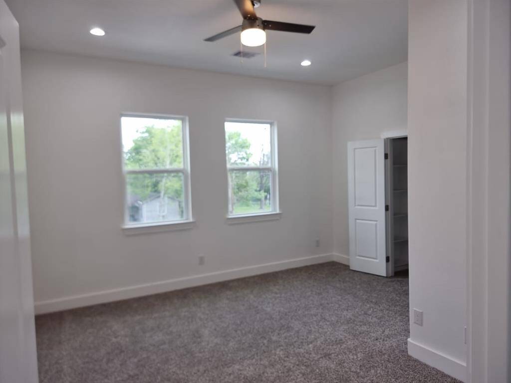 This bright, spacious room features two large windows, plush carpet, and a ceiling fan with recessed lighting. It also includes a closet with a white door, perfect for storage.