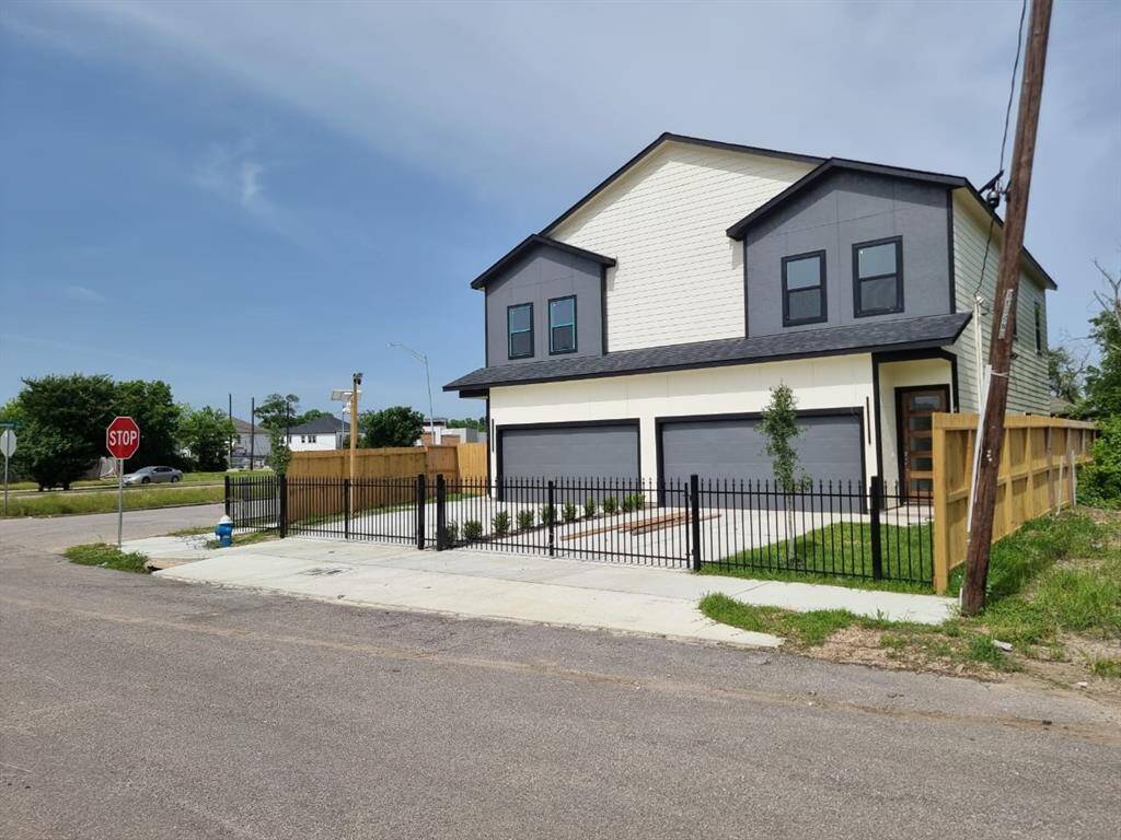 Modern duplex with a sleek exterior, featuring two stories, two garages, and fenced front yards. Located on a corner lot with a stop sign and nearby greenery.