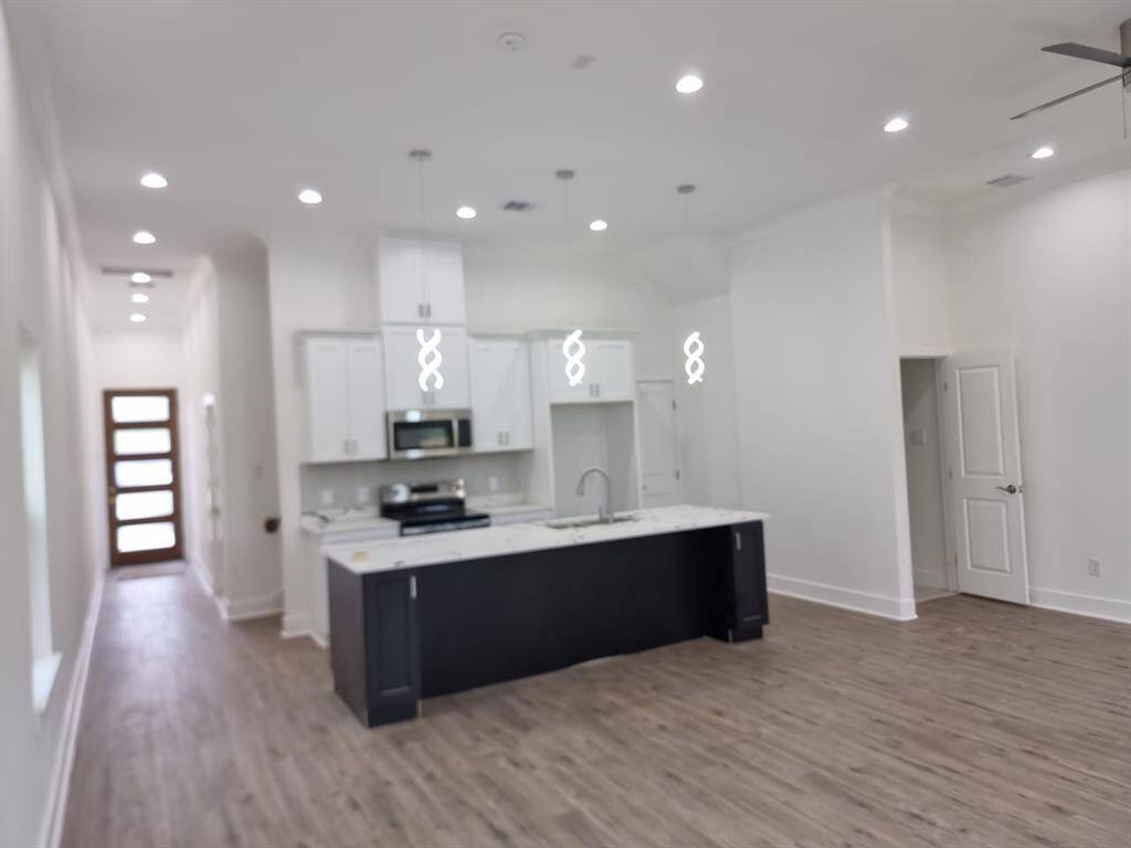 This spacious, modern kitchen features an open layout with sleek cabinetry, a large island with a sink, stainless steel appliances, and elegant pendant lighting. The light wood flooring and recessed lighting create a bright and airy atmosphere.