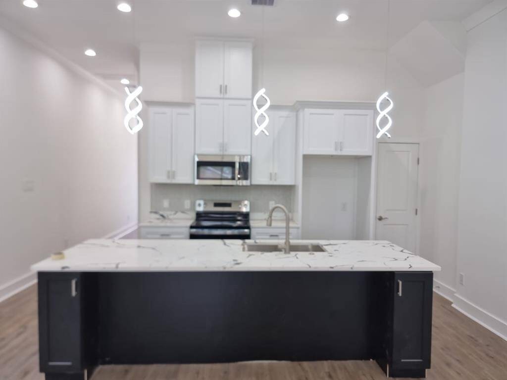 Modern kitchen with sleek white cabinets, stainless steel appliances, and a large marble island. The room is well-lit with stylish pendant lights and features hardwood flooring.