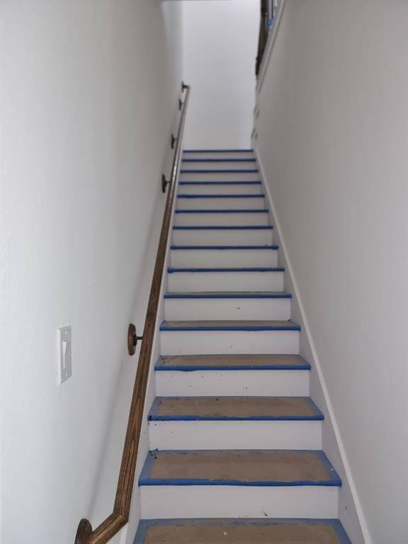 A narrow, white staircase with wooden handrails on both sides leads upward, featuring blue tape along the edges for protection or painting purposes.