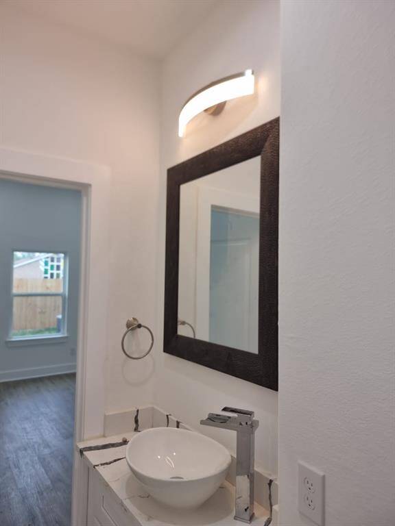 Modern bathroom with a stylish vessel sink, sleek faucet, and a large framed mirror. Bright lighting and a view into a room with wood flooring and a window.
