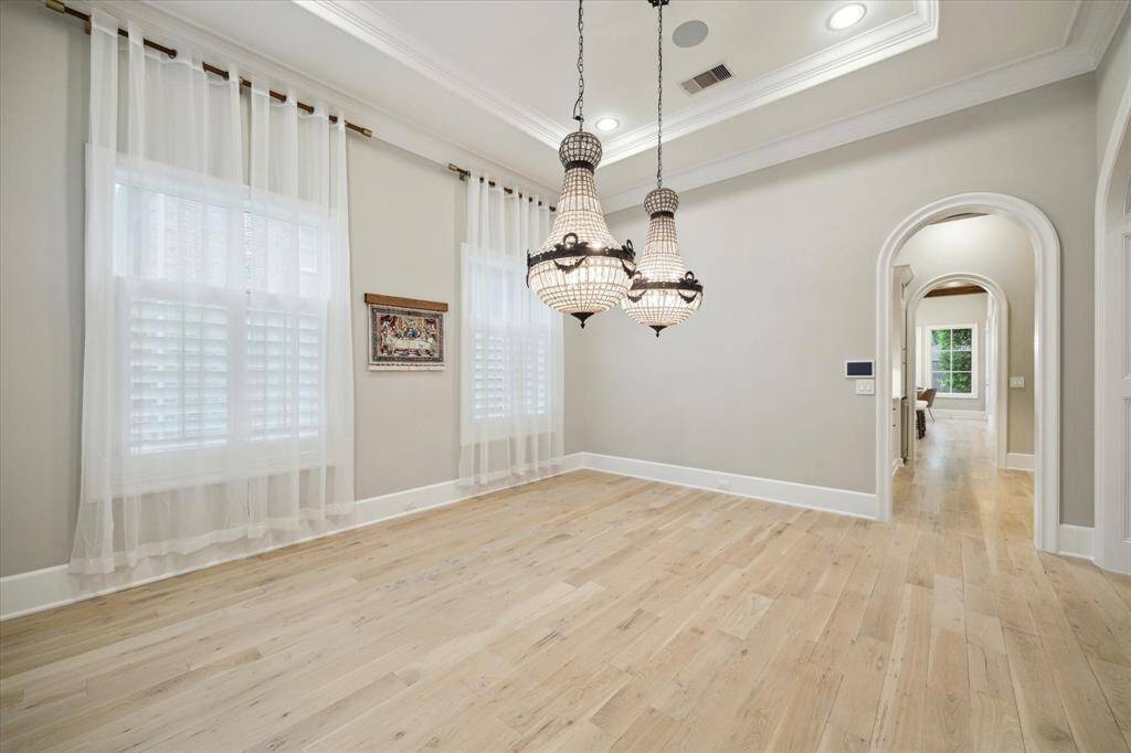 Elegant traditional formal dining room, featuring light wood flooring that exudes sophistication. The room is adorned with dual chandeliers, casting a soft, inviting glow that enhances the luxurious atmosphere.