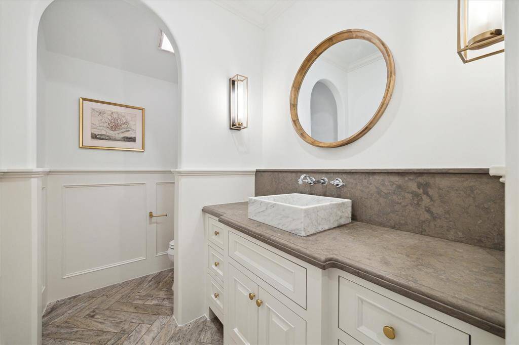 The formal half bath is a true standout, featuring custom raised wood-block wainscoting that adds a touch of elegance. Decorative herringbone-patterned tile flooring complements the beautiful countertop, while a raised sink paired with wall-mounted fixtures creates a chic focal point.