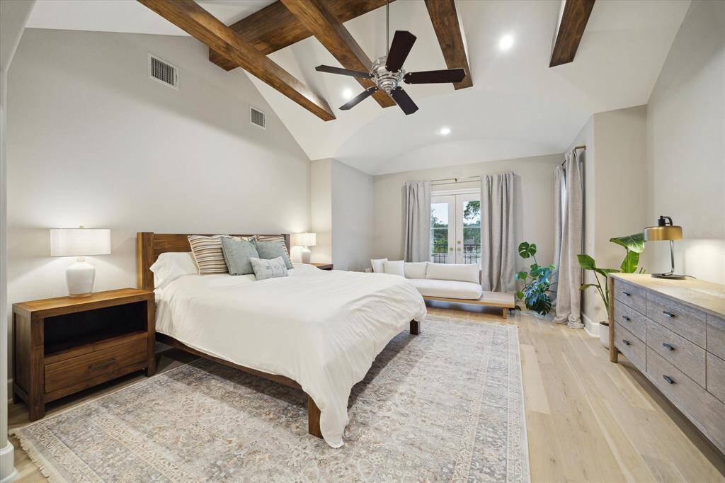 The primary suite offers a breathtaking retreat, featuring a vaulted ceiling adorned with cross wood beams that add architectural interest. A charming Juliette balcony overlooks the serene backyard.