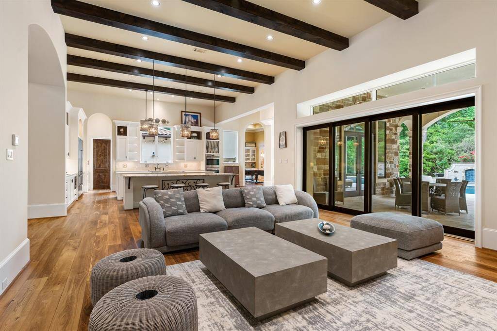 Neutral-toned walls complement the warm wood flooring and decorative ceiling beams overhead, while a transom window above the sliding glass doors fills the space with abundant natural light.