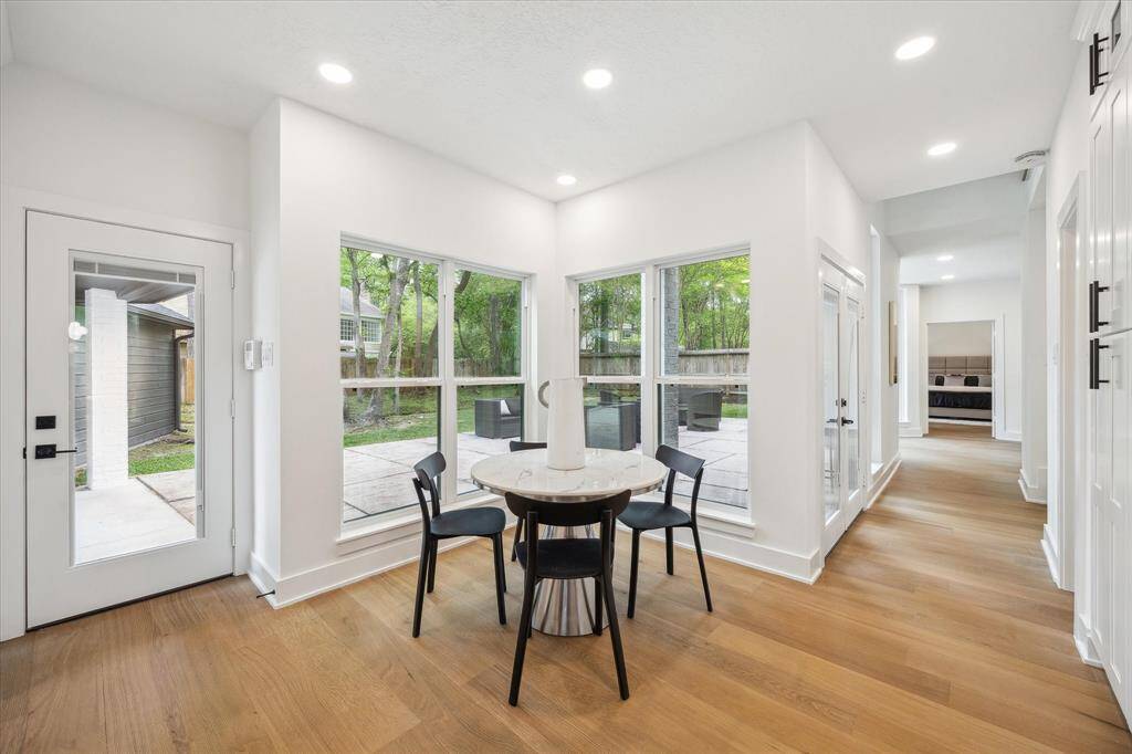 This photo features a bright, modern breakfast room with large windows offering a view of a lush backyard.