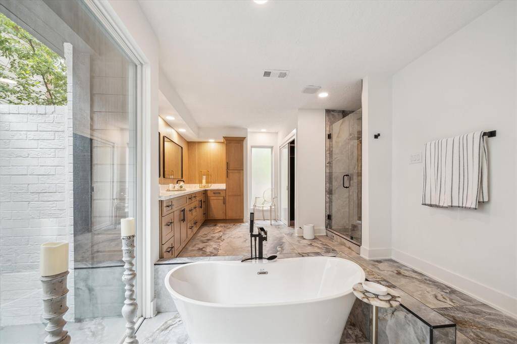 This is a spacious, modern bathroom featuring a freestanding tub, large vanity with dual sinks, and a glass-enclosed shower. Natural light pours in through a large window, enhancing the airy feel. Elegant finishes and sleek fixtures add a touch of luxury.