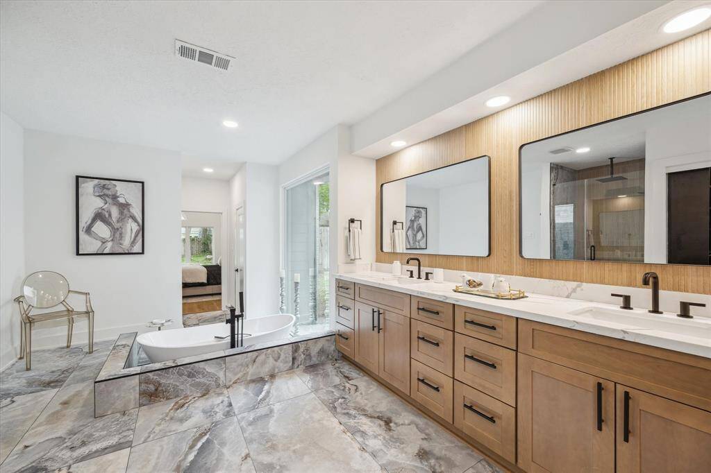 The bathroom features a modern design with  large walk-in shower. It has dual vanities with ample storage, elegant fixtures, and stylish tile flooring.