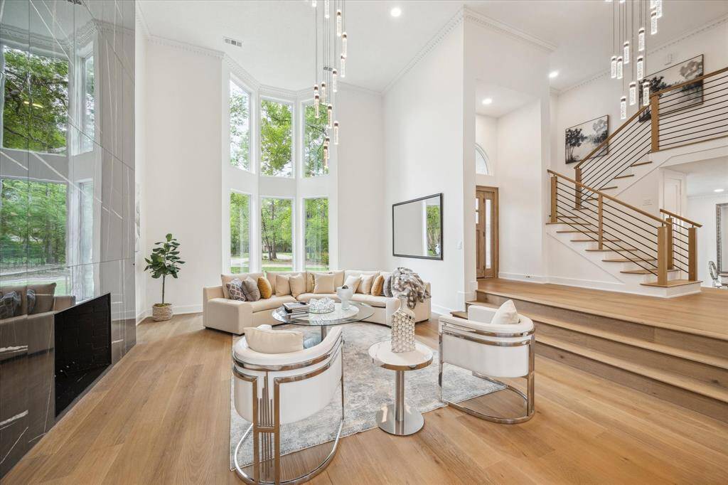 This spacious living room features high ceilings and large windows that flood the space with natural light. The modern, open design includes a stylish staircase, sleek fireplace, and a cozy seating area, creating an inviting and elegant atmosphere.
