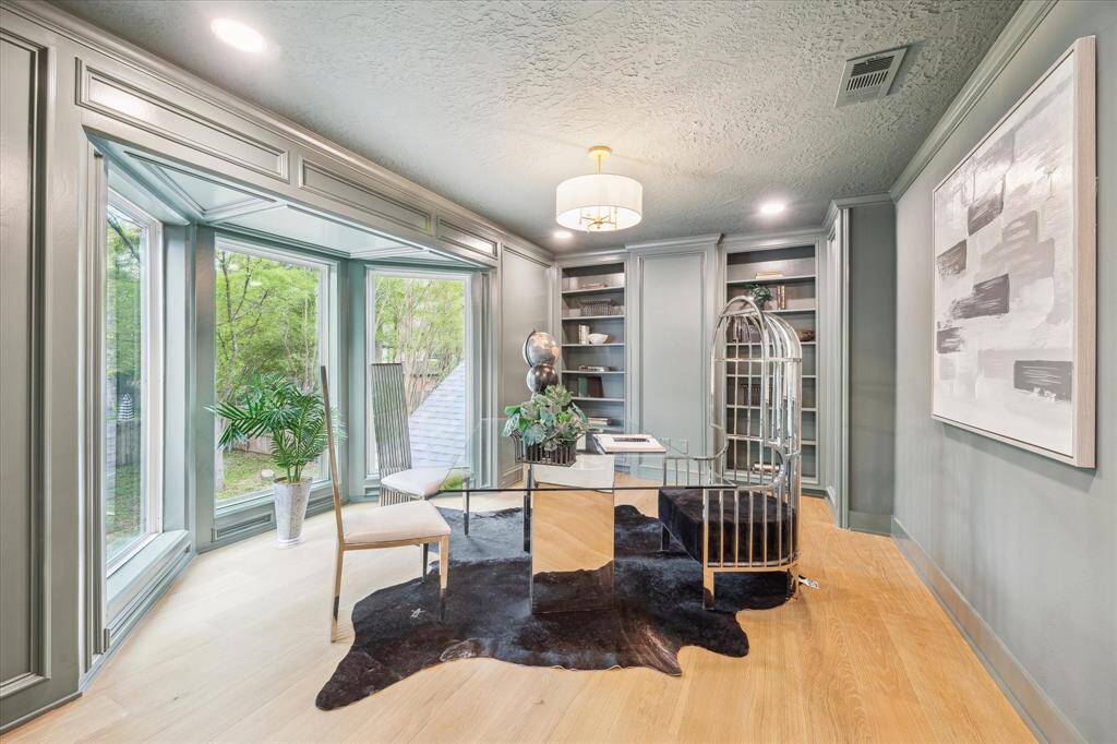 This photo features a stylish home office with large bay windows offering plenty of natural light. The room is painted in a soft green with elegant paneling and built-in shelves creating a sophisticated and inviting workspace.  Option to make this the 5th bedroom, exercise room or use as you desire.