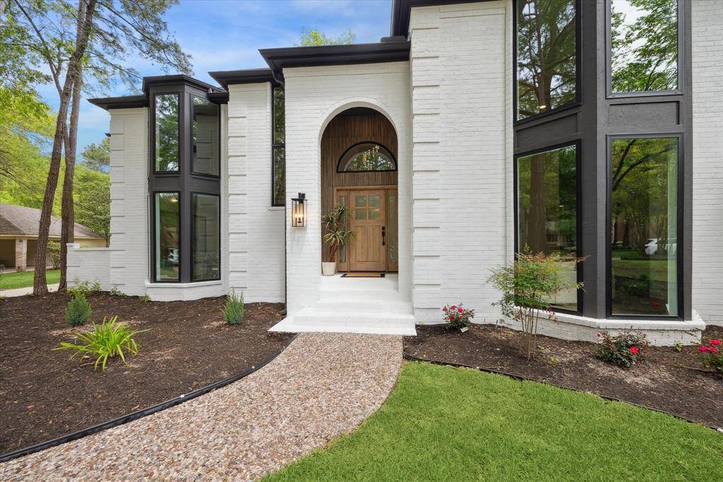 This home features a modern exterior with large windows and a welcoming wooden front door. The landscaped front yard includes a stone path and fresh greenery, creating an inviting entrance.