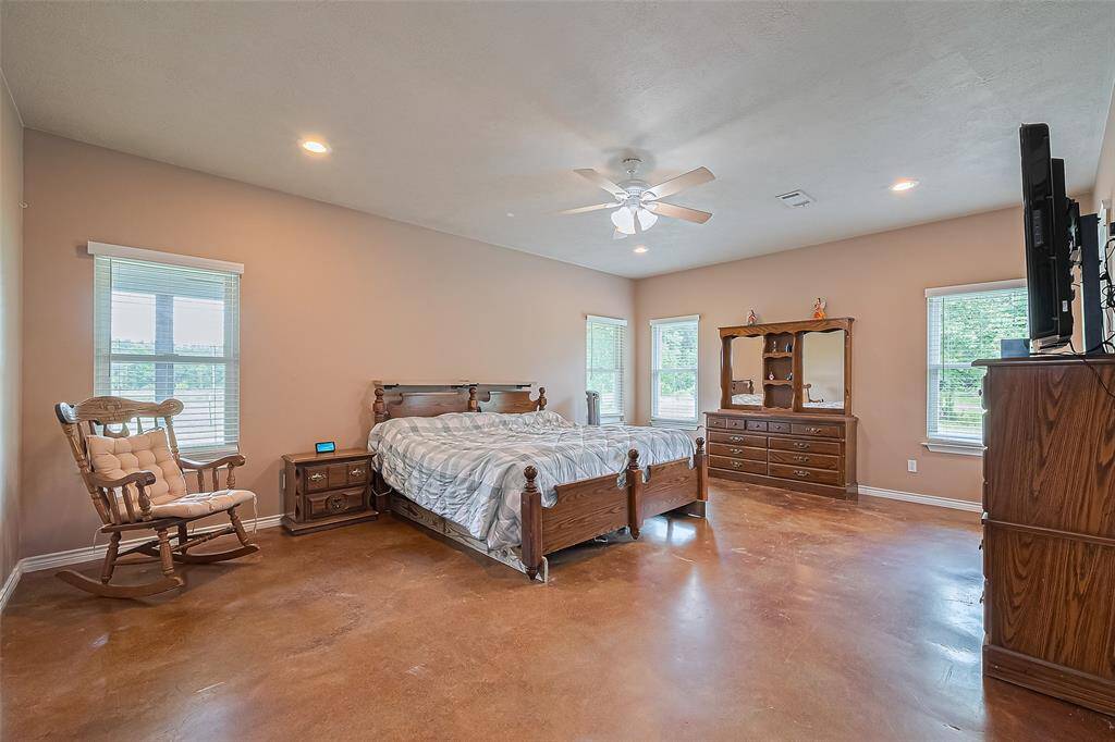 Daylight streams through multiple oversized windows, while recessed lighting and a ceiling fan add comfort and ambiance to this restful space.