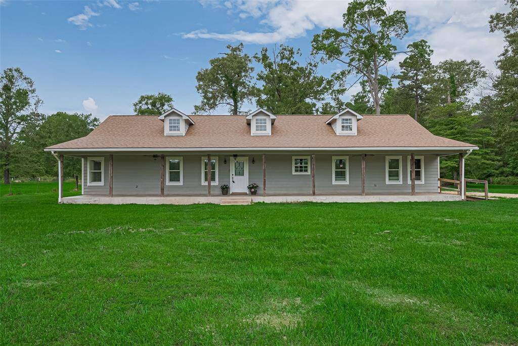 Set against a backdrop of open green space, the home presents a striking facade with a full-length porch and trio of dormer windows, adding charm and character to the wide footprint.