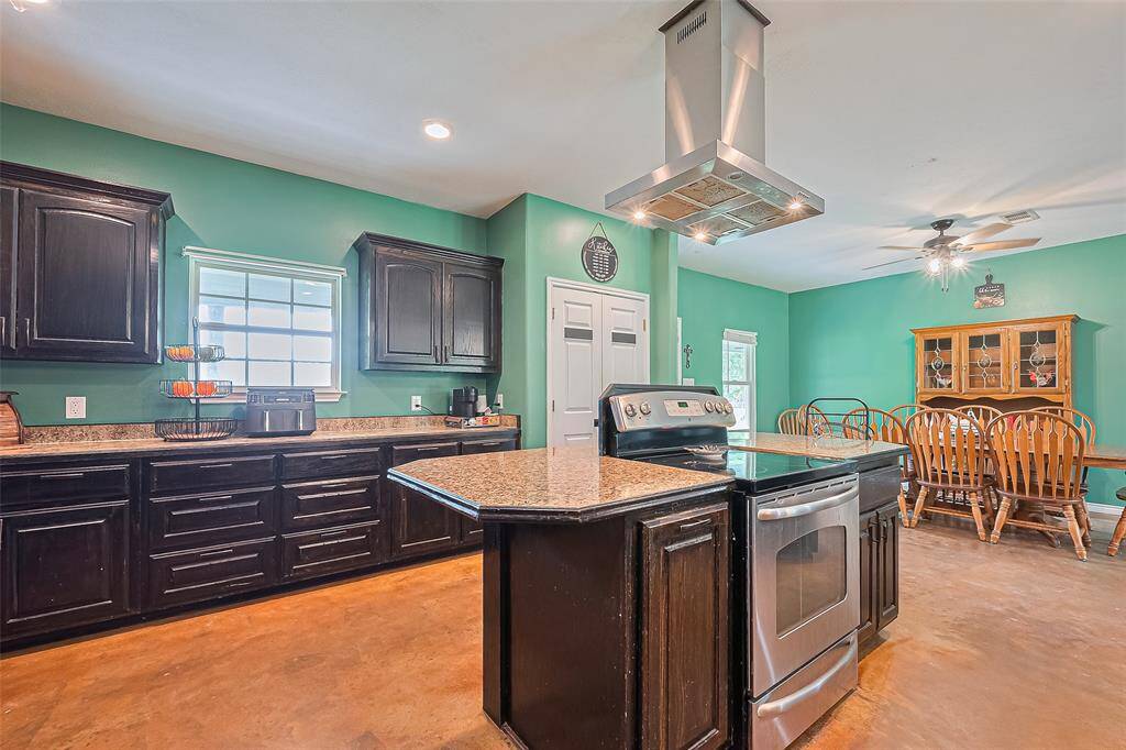 The kitchen features a central island with a built-in range and overhead exhaust. A large window welcomes natural light, while the adjacent dining area makes the layout convenient and connected.