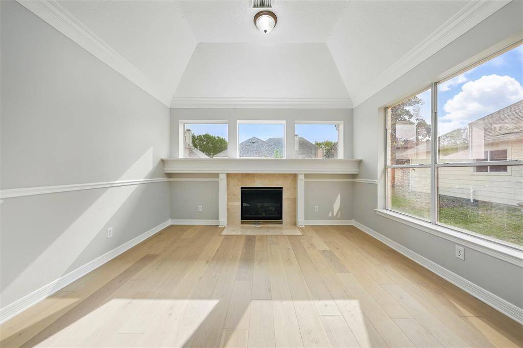 This room features a high ceiling, light hardwood floors, and a central fireplace. Large windows provide ample natural light, creating a bright and inviting atmosphere.