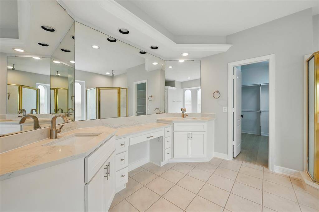 This spacious bathroom features a dual-sink vanity with elegant newly quatz countertops, a large mirror, and ample storage. The room is bright and airy, with neutral tones and a walk-in closet visible through an open doorway.