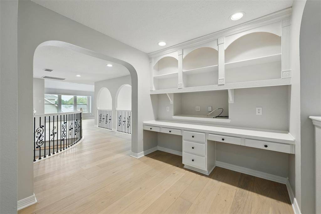 This is a bright, open landing area with light wood flooring and elegant railing. It features a built-in desk with overhead shelving, ideal for a home office or study nook, and is well-lit with recessed lighting.