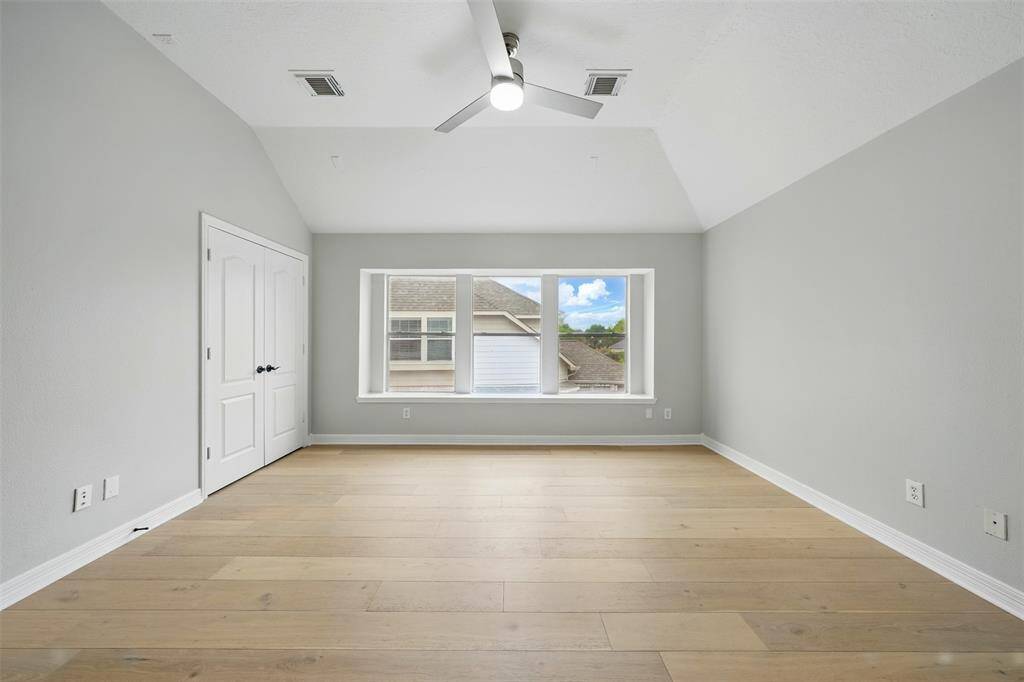 Spacious, light-filled game room with light wood flooring, neutral walls, and a ceiling fan. Features a large window with a view and a double-door closet.