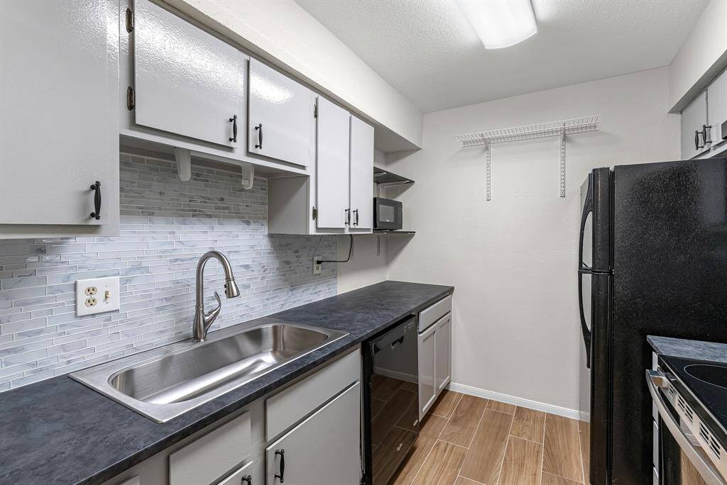 This modern kitchen features sleek gray cabinetry, a stylish tile backsplash, and appliances. The compact layout maximizes space, offering ample storage and a functional design.
