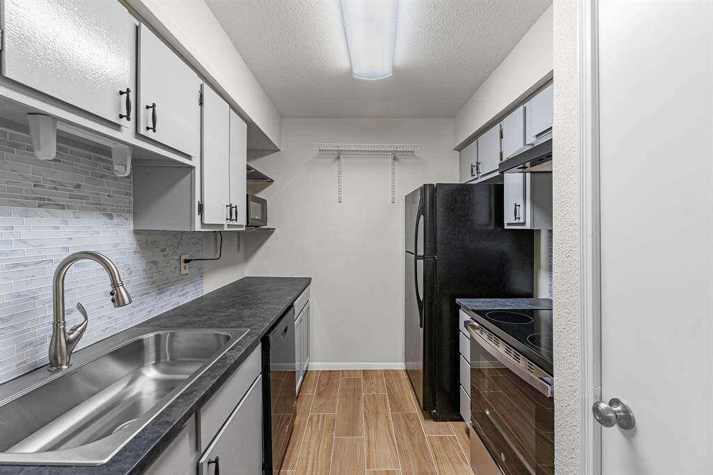This kitchen features a sleek, compact design with modern appliances, an oversized sink, and ample cabinet space. The backsplash is stylishly tiled, and the wood-look flooring adds warmth to the space. Perfect for efficient cooking and storage.