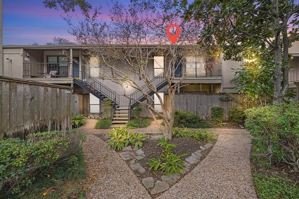 This charming upstairs condo is surrounded by lush greenery and a well-maintained garden path. The exterior has a cozy, inviting feel with a mix of natural wood and modern design elements, perfect for a tranquil living experience.