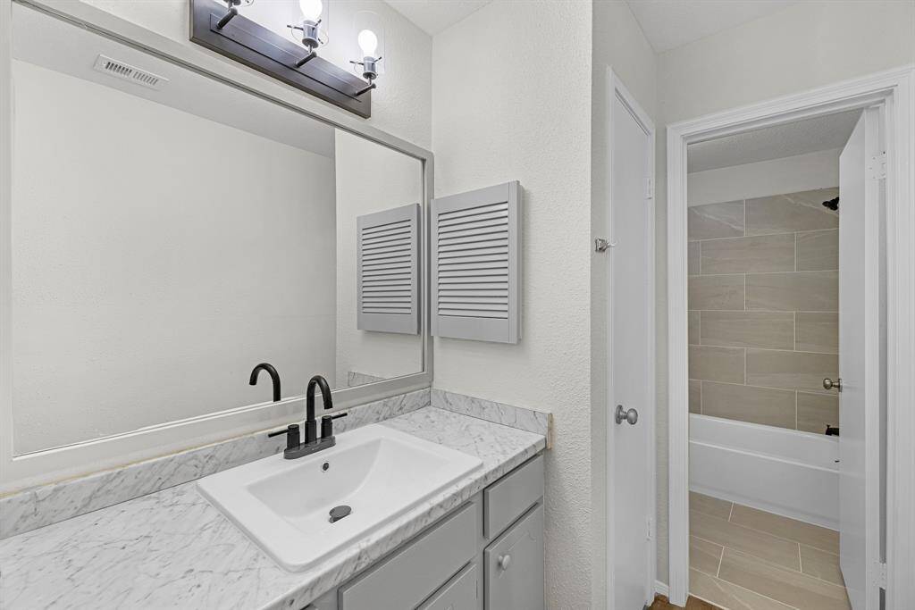 Modern bathroom with a sleek marble countertop and an under-mount sink. Featuring a large mirror, contemporary lighting, and modern tile work in the shower area, creating a clean and inviting space.