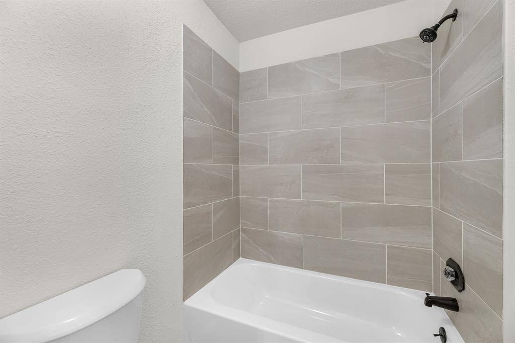 Bathroom features a modern tub and shower combo with sleek gray tile surround and elegant dark fixtures, offering a clean and contemporary look.