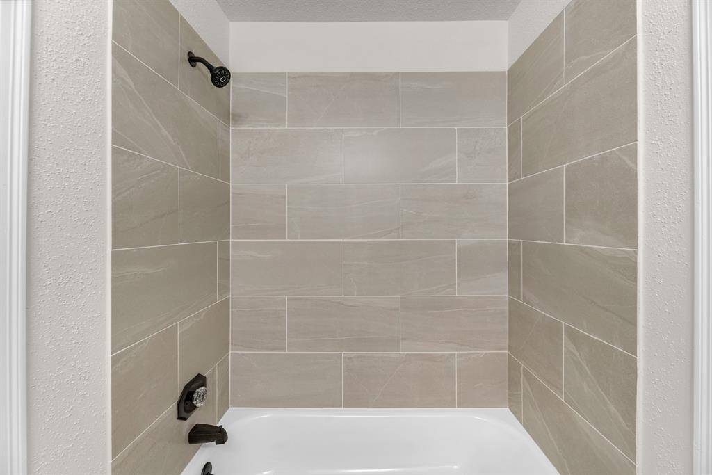 Contemporary shower recently remodeled with large-format tile walls and a white bathtub. The fixtures are dark, providing a modern contrast. The design is clean and minimalist, ideal for a stylish bathroom.