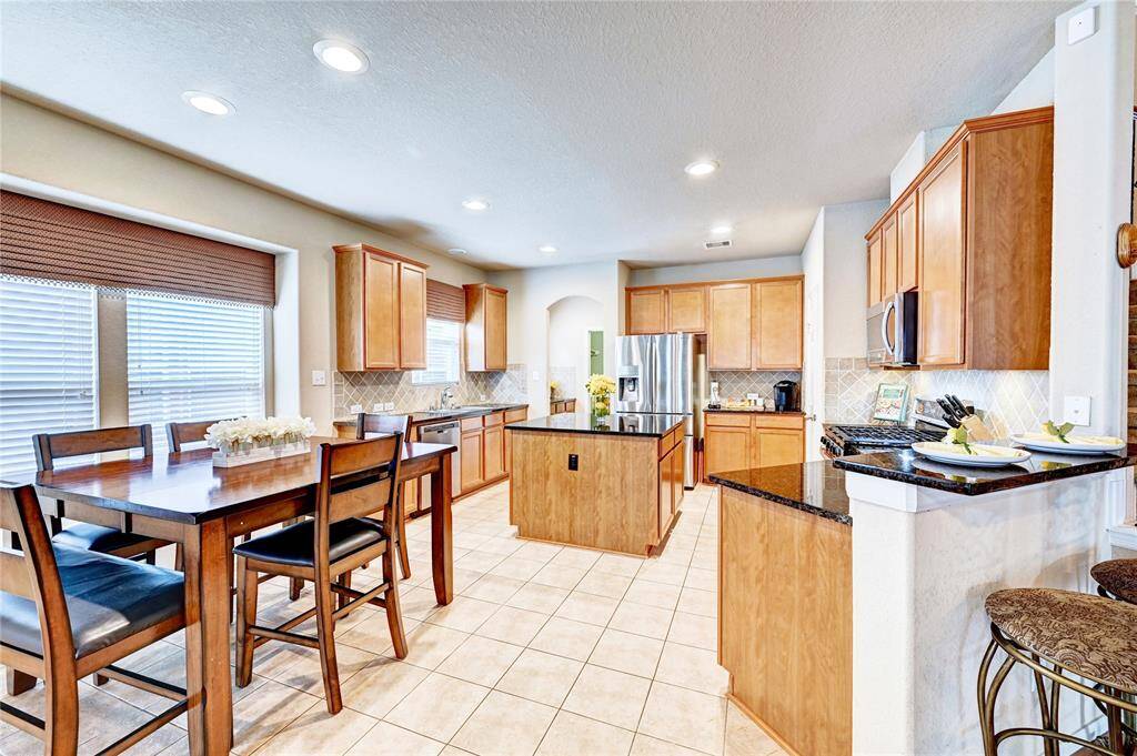 Spacious kitchen with modern stainless steel appliances, granite countertops, and ample cabinetry. Features a central island, tile flooring, and an adjacent dining area with large windows for natural light.