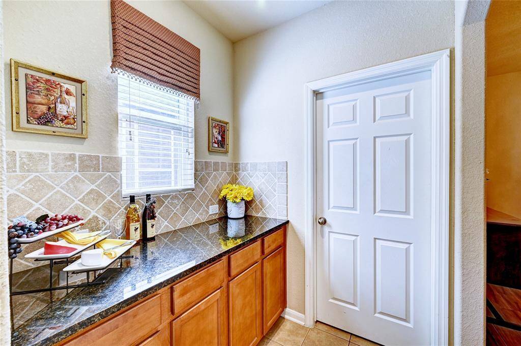 This photo showcases a charming kitchen nook with granite countertops, light wood cabinetry, and decorative tile backsplash. It includes a window with natural light. The door leads to the inside laundry room.