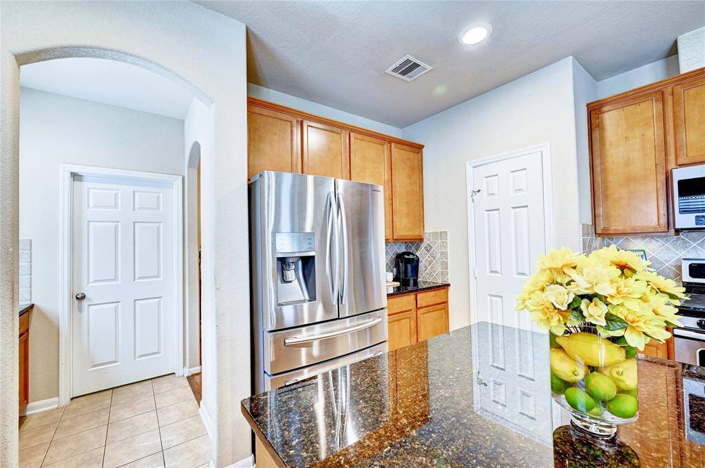 Bright, modern kitchen with stainless steel appliances, granite countertops, and wooden cabinetry. Features include a spacious island, tile flooring, and recessed lighting.