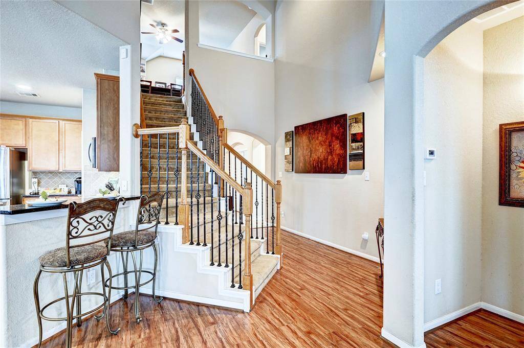 This welcoming home features an open floor plan with a staircase highlighted by elegant wrought iron railings. The space is enhanced by warm wood flooring, a cozy breakfast bar with seating, and modern kitchen cabinetry. Natural light and tasteful decor complete the inviting atmosphere.