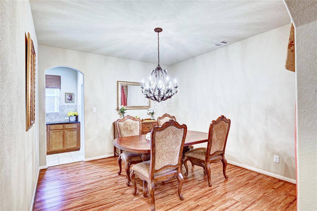 This dining area features elegant wooden flooring, a classic chandelier, and a cozy setup. An archway leads to the kitchen nook, enhancing the space's openness.