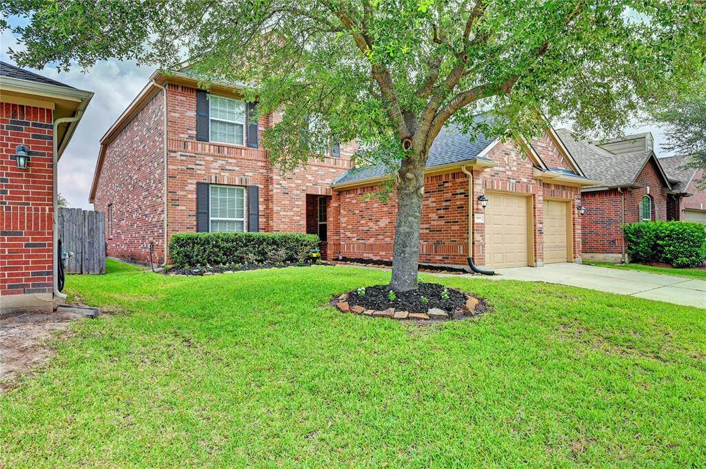 Charming two-story brick home with a well-maintained front lawn and a mature tree. Features a two-car garage and a welcoming entryway.