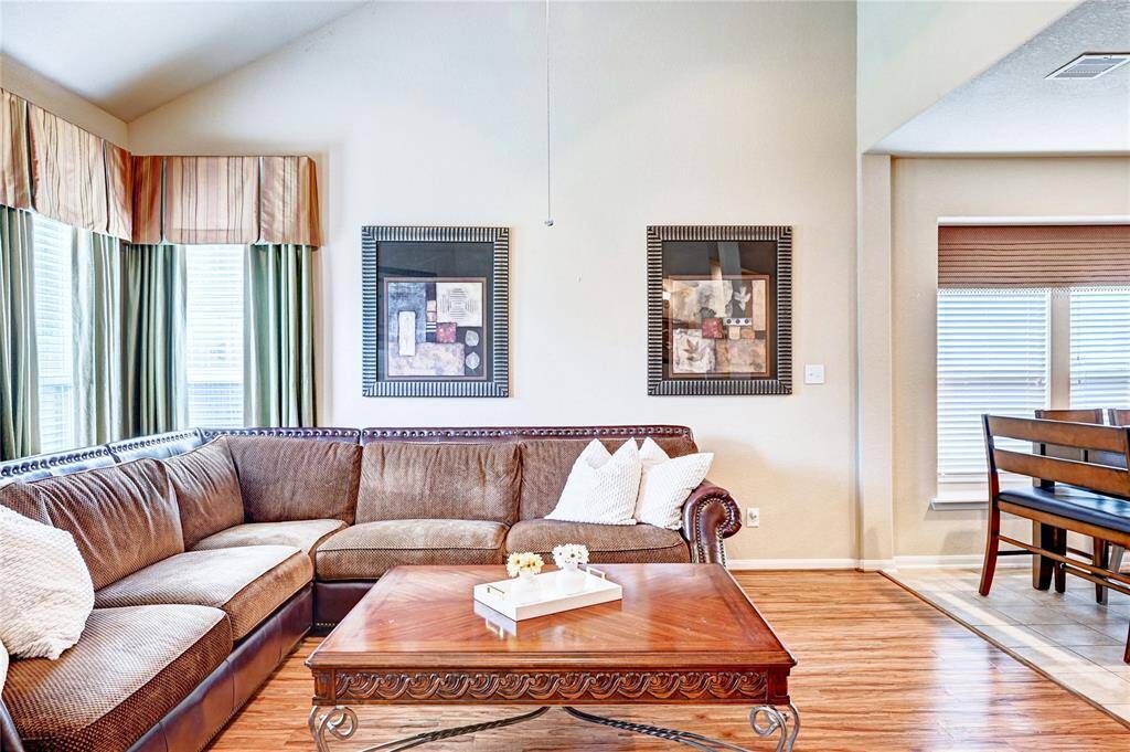 Bright and inviting living space featuring a large sectional sofa, elegant coffee table, and stylish artwork. Natural light floods in through the windows, highlighting the open layout with adjoining dining area.