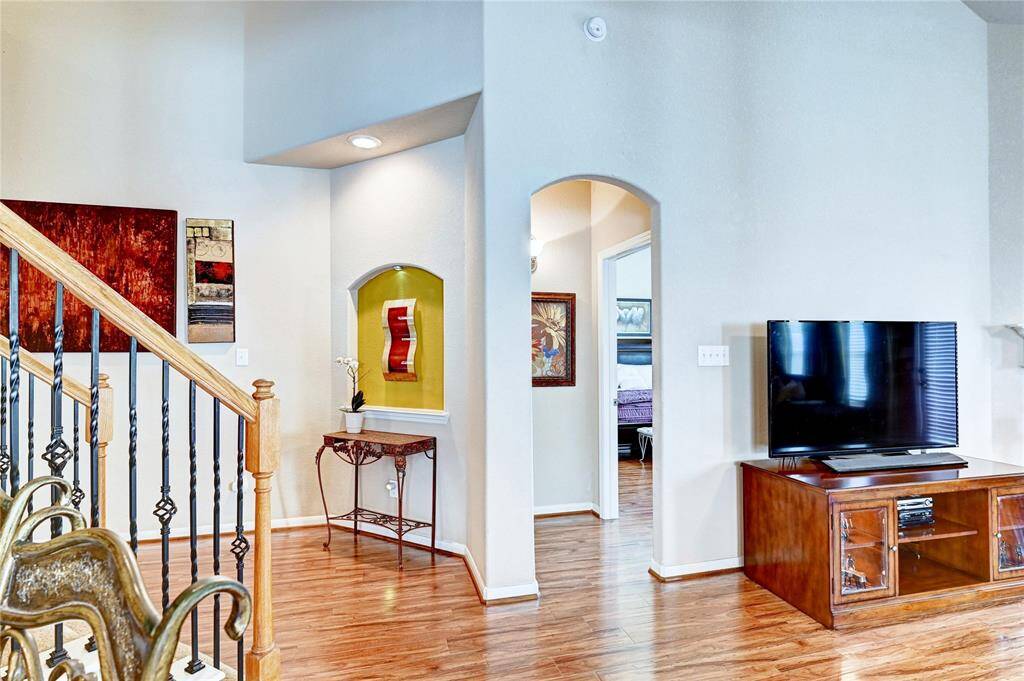 This inviting living space features warm hardwood floors, a stylish staircase with wrought iron detailing. An arched doorway leads to the primary bedroom, while a built-in niche adds character. The room offers a cozy yet modern atmosphere.