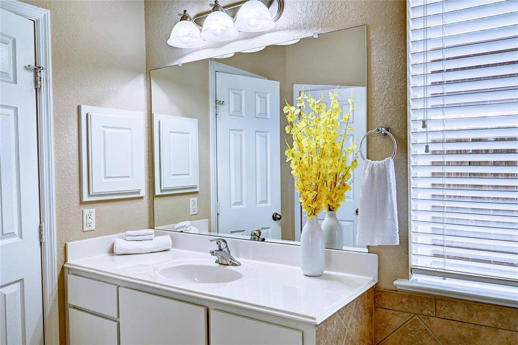 Bright and inviting bathroom with a clean white vanity, modern fixtures, and ample natural light from a window with blinds. The space creates a fresh and welcoming atmosphere.