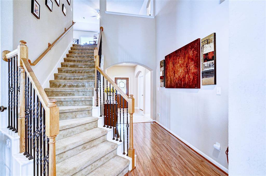 This photo showcases a bright, inviting entryway with a staircase featuring wooden railings and iron balusters.