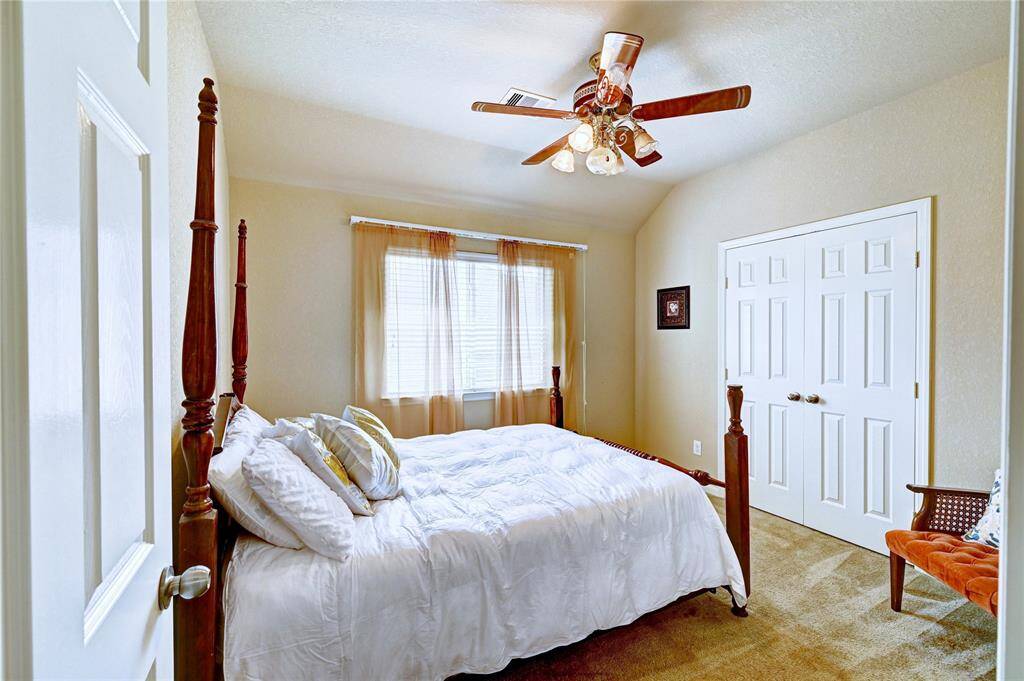 This cozy bedroom has a ceiling fan. Natural light streams through the window and there's ample closet space with double doors. A small seating area adds comfort to the warm, inviting space.