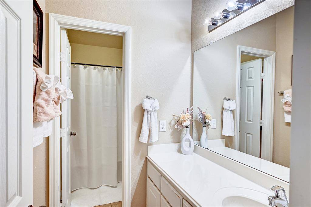 This bathroom features a clean, modern design with a large mirror, a vanity with ample counter space, and a bright, well-lit atmosphere. The shower is enclosed with a curtain for privacy, and tasteful decor adds a touch of elegance.