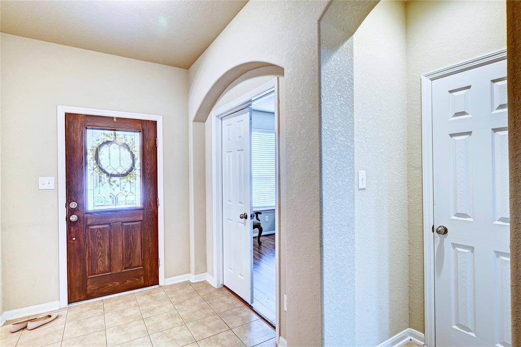 This entryway features a wooden front door with decorative glass, tile flooring, and an archway leading to your home office. It has a warm, welcoming feel.