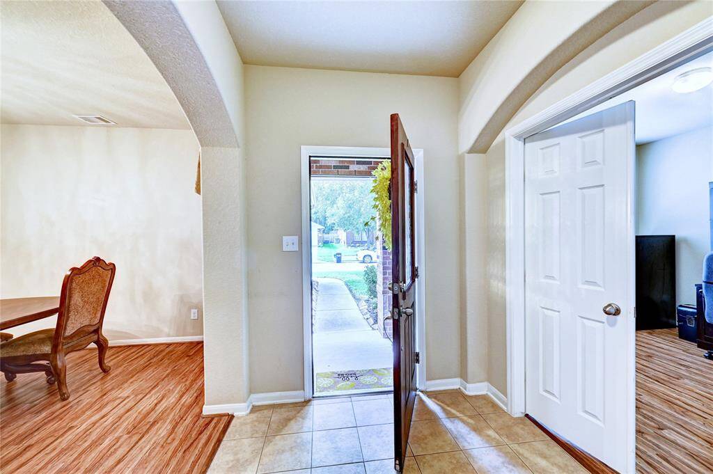 The photo shows a welcoming entryway with tiled flooring, an open front door, and archways leading to the your home office and adjacent to the formal dining room. The space is bright and inviting.