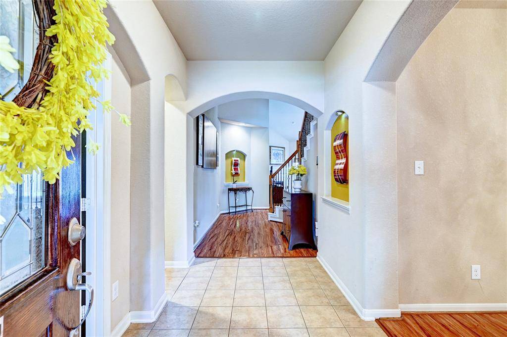 This inviting entryway features a mix of tile and hardwood flooring, leading to a staircase. Arched doorways add elegance, while decorative niches provide charm. The space is bright and welcoming, perfect for a warm home arrival.