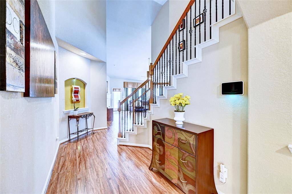 This photo showcases a bright and inviting entryway with wood flooring and a stylish staircase featuring iron railings. The space is accented with modern decor and artwork, offering a welcoming first impression.